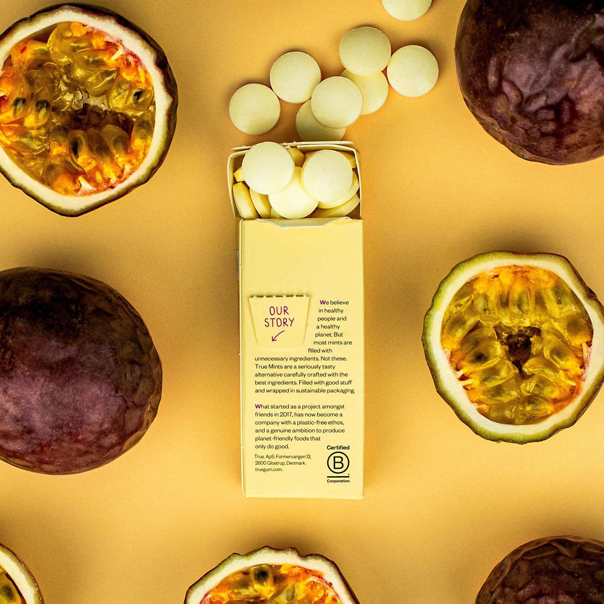 True Mints Passionsfrucht Schachtel offen in Rückansicht, Pastillen sind sichtbar und ganze und halbierte Maracujas 